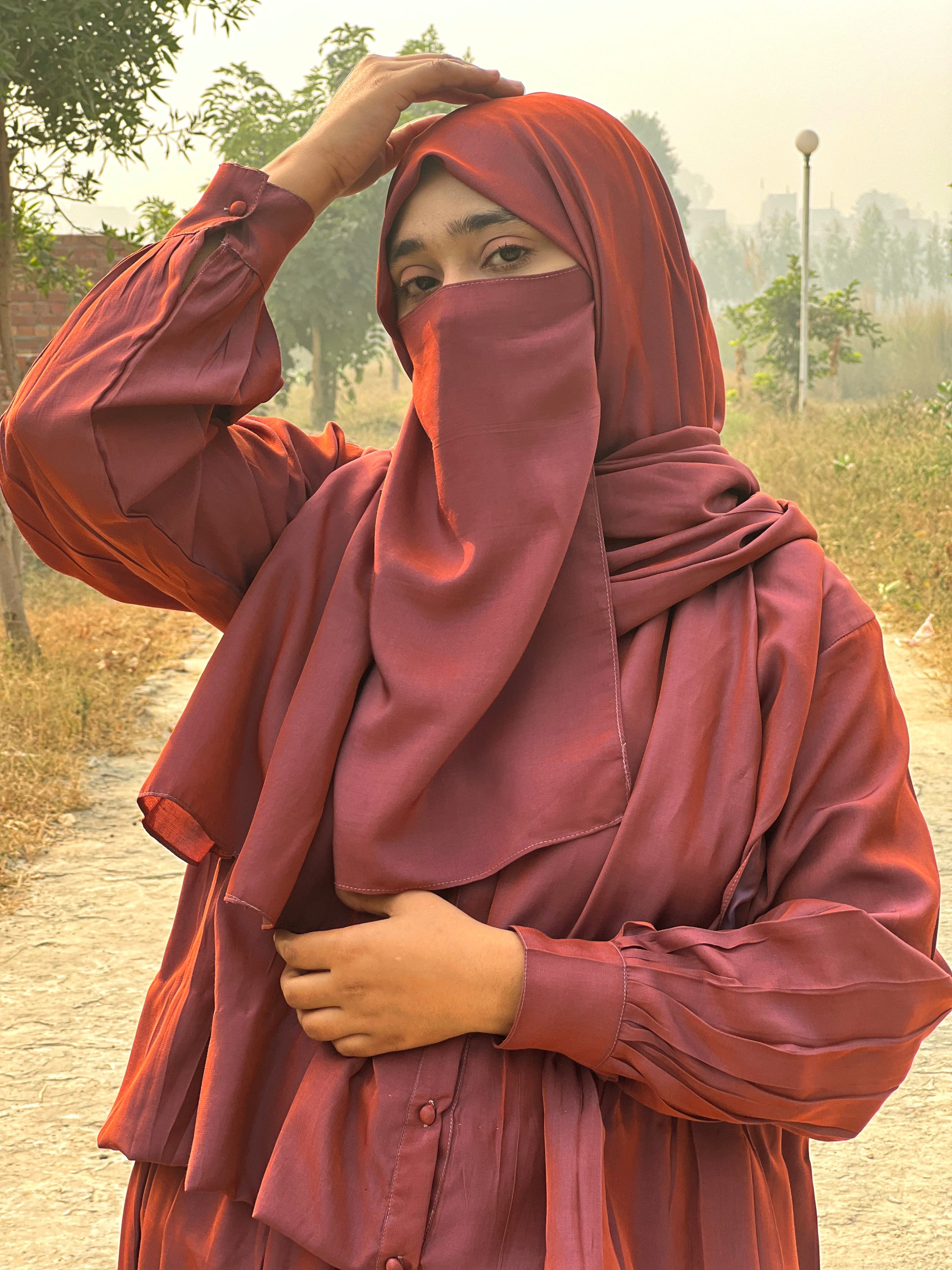 Person wearing a maroon outfit with a headscarf outdoors.